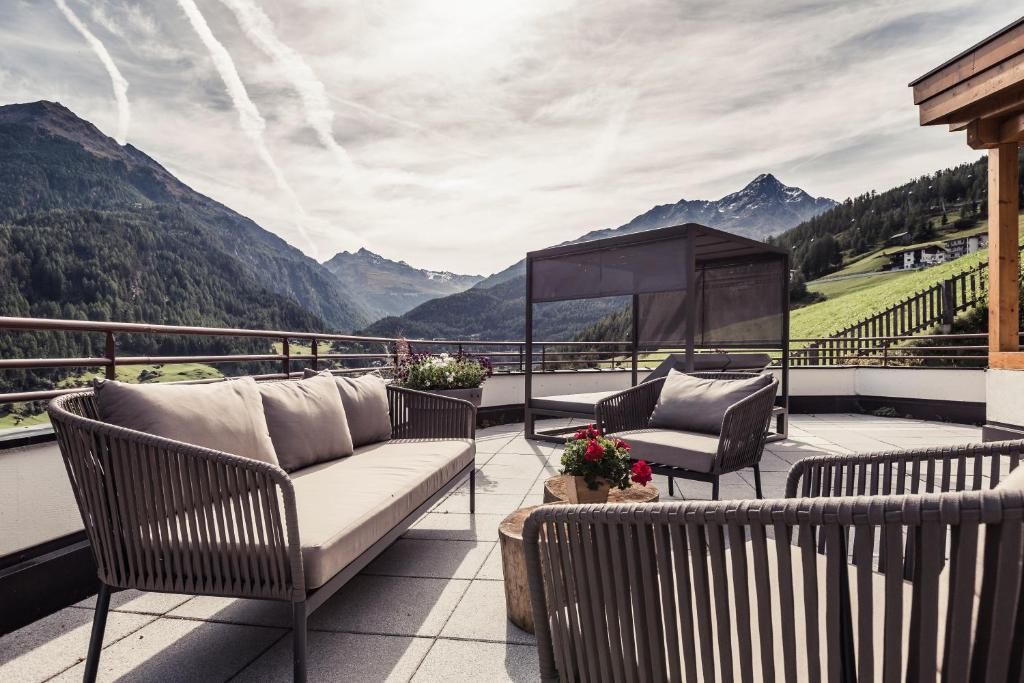 Una terraza con mobiliario de mimbre, una zona de estar cubierta y vistas a las montañas.