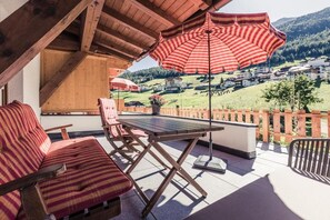 Een terras buiten met een tafel en stoelen, een grote gestreepte parasol en een uitzicht op een dorp op de achtergrond.