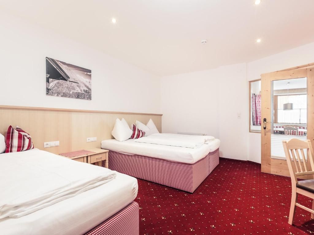 Habitación de hotel con dos camas, cabecera de madera, alfombra roja, una mesita y una silla.