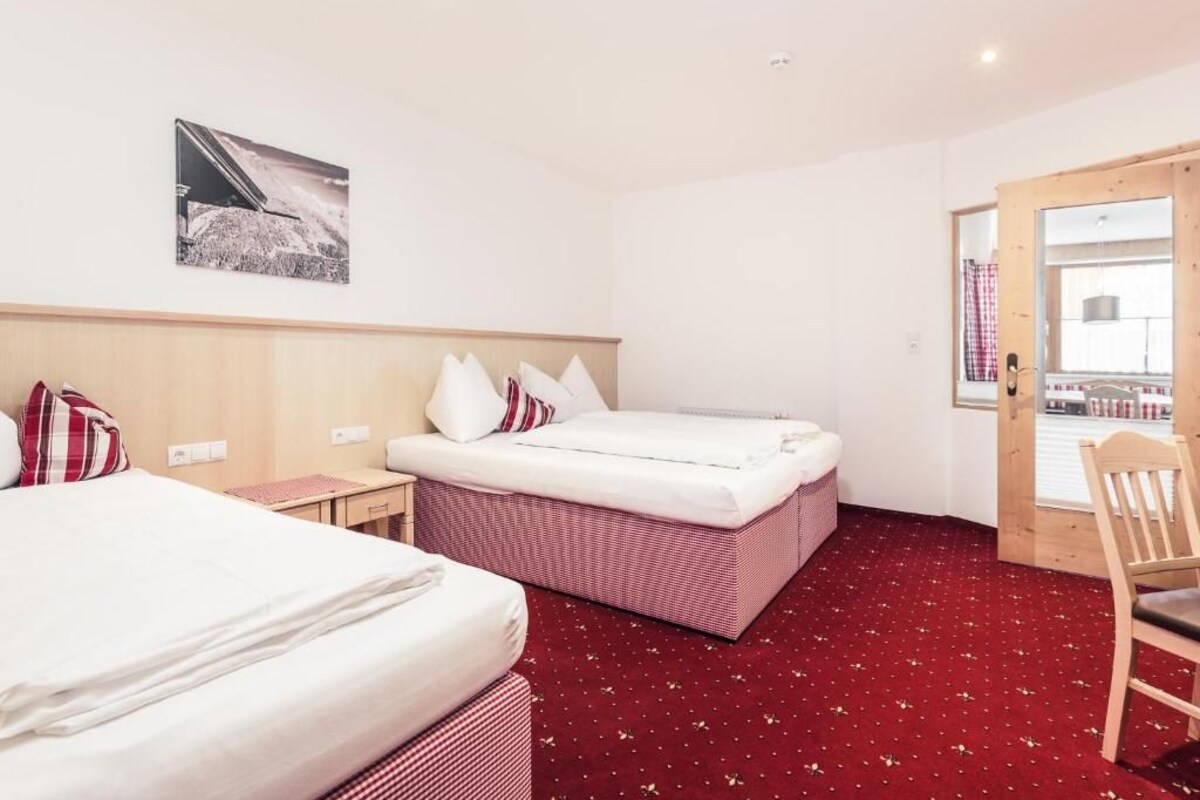Een hotelkamer met twee bedden, een houten hoofdbord, een rood tapijt, een klein tafeltje en een stoel.