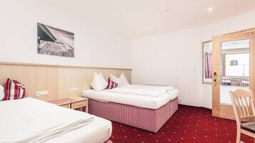 Habitación de hotel con dos camas, cabecera de madera, alfombra roja, una mesita y una silla.