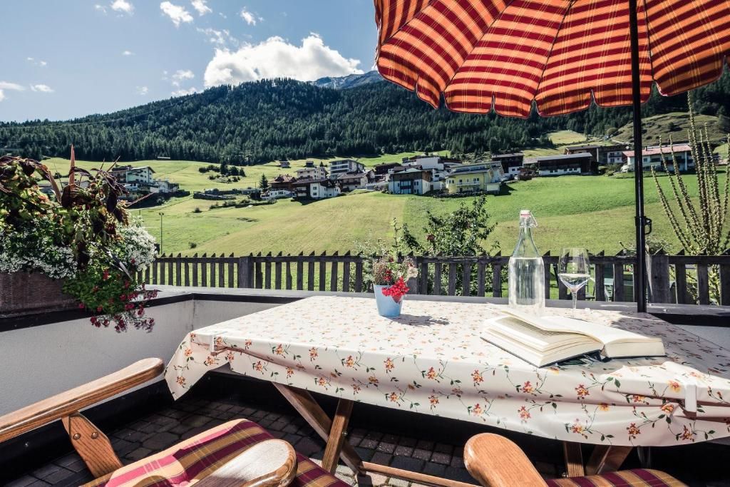 Een tafel met een tafelkleed met bloemen, een boek, een glas wijn en een gestreepte parasol.