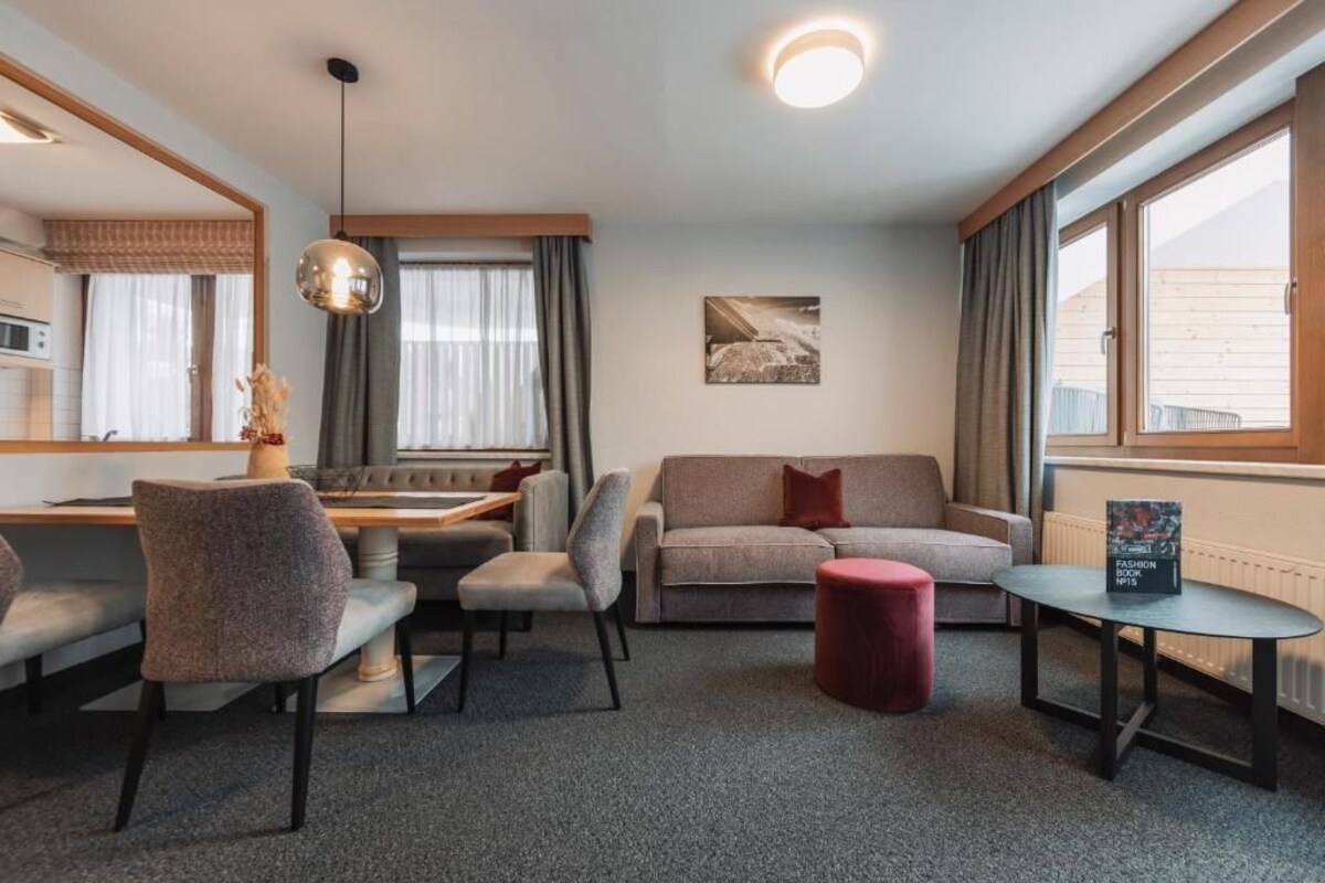 Een moderne woonkamer met een bank, stoelen, een eettafel en een rode poef.