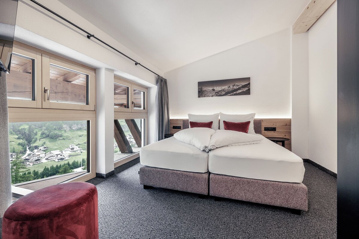 Een moderne slaapkamer met een groot bed, uitzicht op een dorp door de ramen en een houten hoofdeinde.