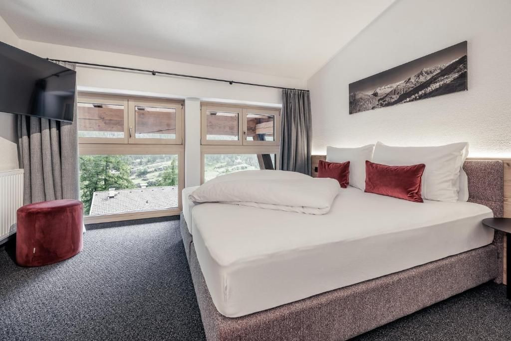 Ein modernes Hotelzimmer mit einem großen Bett, einem Flachbildfernseher und einem Fenster mit Blick auf Grünflächen.