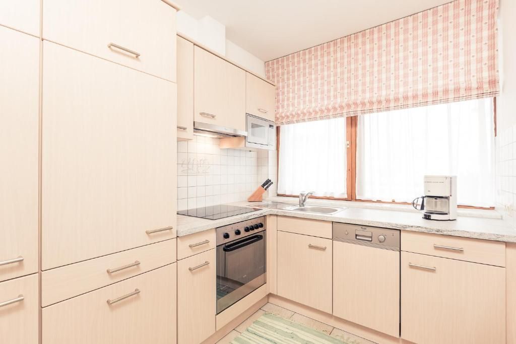 A kitchen with light-colored cabinets, a microwave, an oven, a dishwasher, and a window with a striped valance.