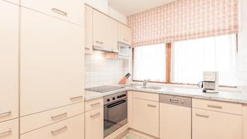 A kitchen with light-colored cabinets, a microwave, an oven, a dishwasher, and a window with a striped valance.