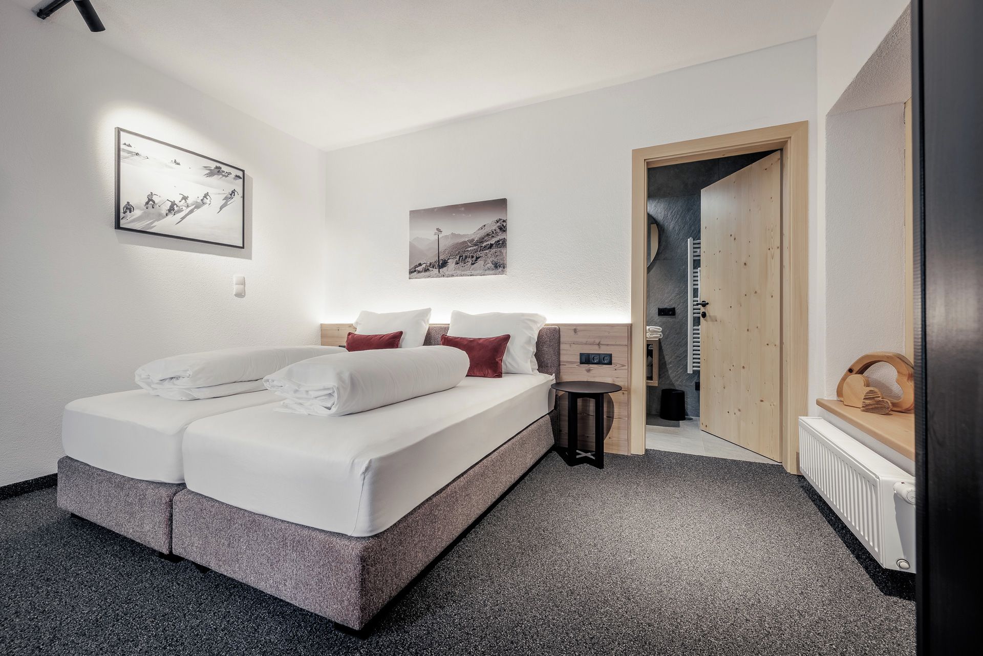 Une chambre moderne avec un lit, une petite table de chevet, une lampe fixée au mur et une porte donnant sur une autre pièce.