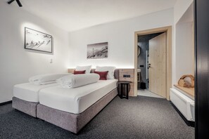 A modern bedroom with a bed, a small bedside table, a wall-mounted light, and a door leading to another room.