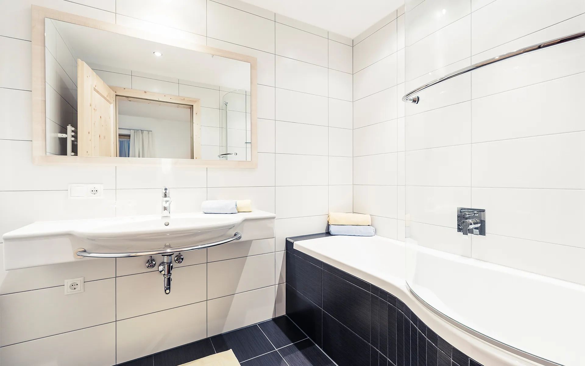 A modern bathroom with a white sink, mirror, and black-tiled shower area.