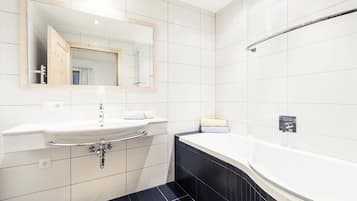 A modern bathroom with a white sink, mirror, and black-tiled shower area.