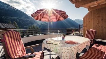 Una terrazza con tavolo e sedie, un ombrellone a righe e vista sulle montagne.