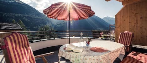 A terrace with a table and chairs, a striped umbrella, and a mountain view.