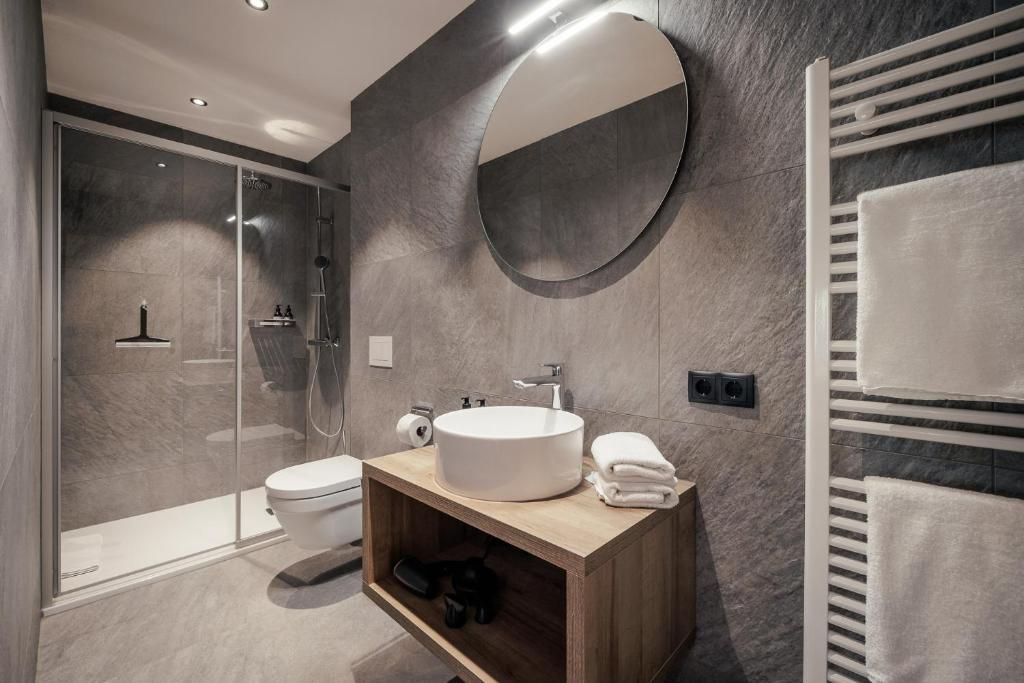 A modern bathroom with a glass-enclosed shower, a wooden vanity with a round sink, and a towel rack.