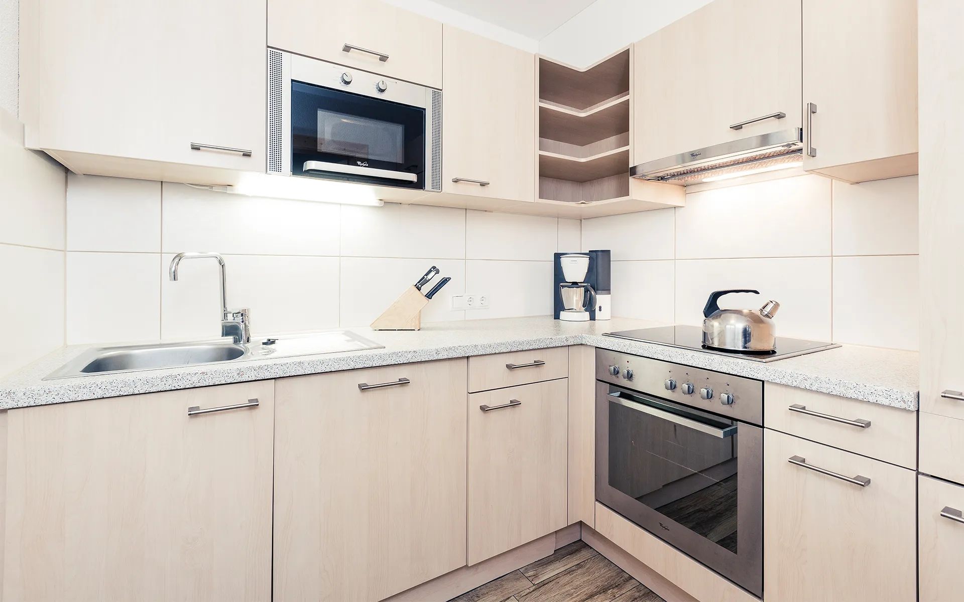 A modern kitchen with a built-in microwave, a coffee maker, and a kettle on the countertop.