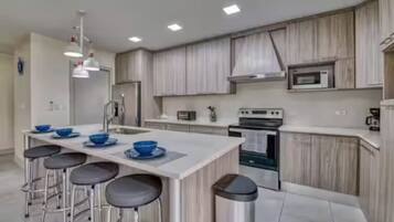 Una cocina moderna con una isla central, taburetes de bar, electrodomésticos de acero inoxidable y armarios de madera clara.