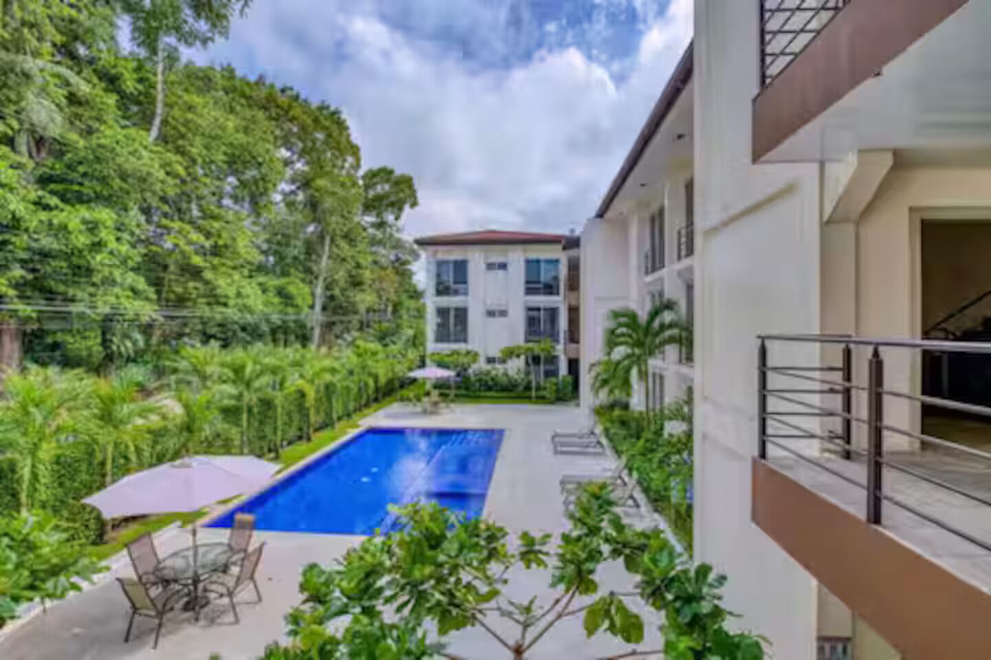 Un edificio residencial con piscina, rodeado de exuberante vegetación y cielo despejado.