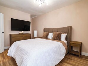 A bedroom with a large bed, a wooden dresser, a bedside table, and a mounted TV. - 2 Makant Street (Bolton)