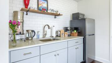 A modern kitchen with white cabinets, a stainless steel refrigerator, a microwave, and a coffee maker.