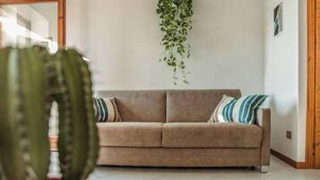 Ein neutral eingerichteter Raum mit einem beigefarbenen Sofa, zwei Kissen und einer hängenden Pflanze.