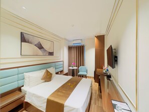 Habitación de hotel con cama, escritorio, silla, televisor y un cuadro en la pared.