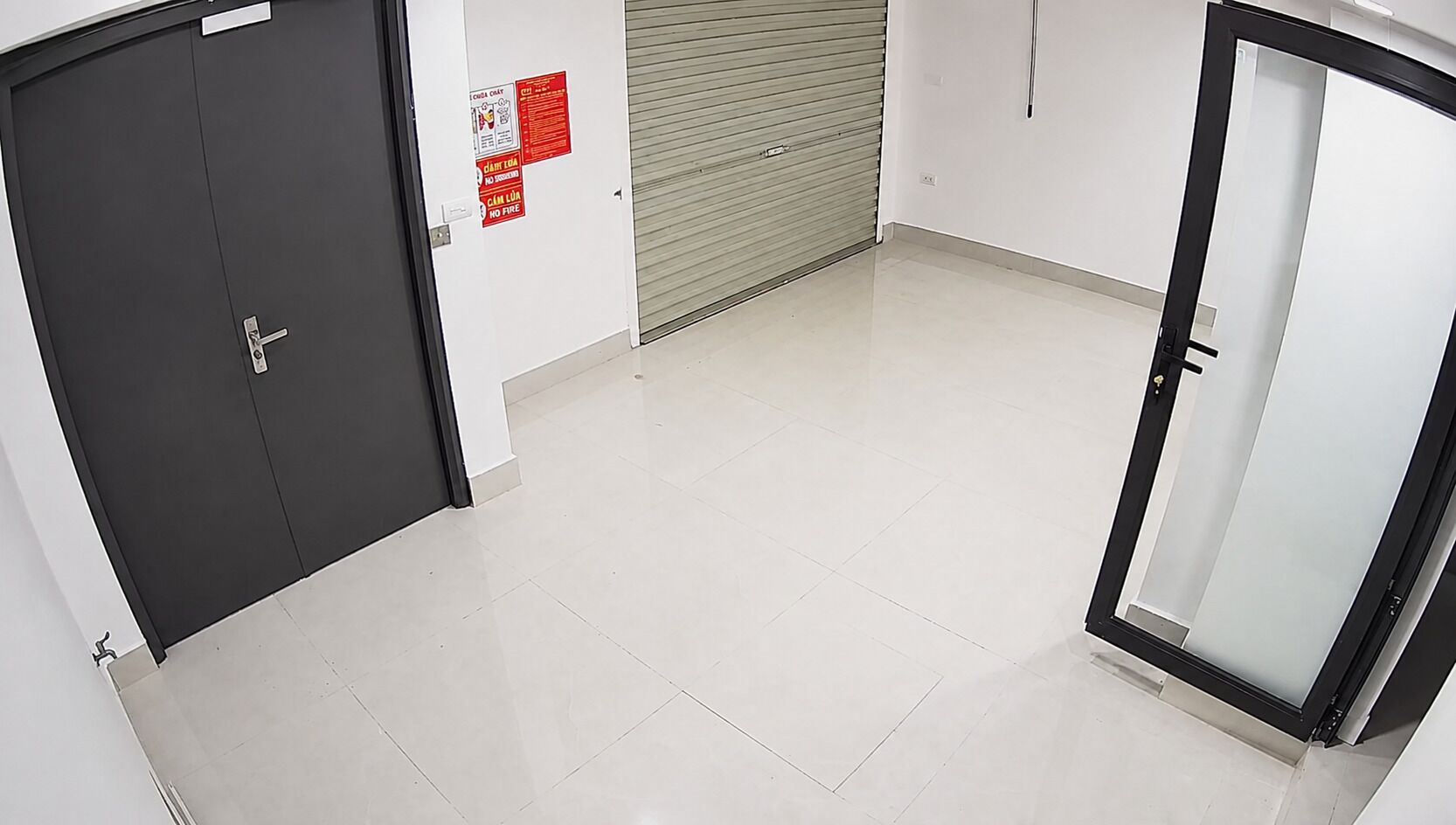 Un couloir avec une porte fermée, un panneau d’information sur la sécurité incendie et une porte de volet roulant fermée.