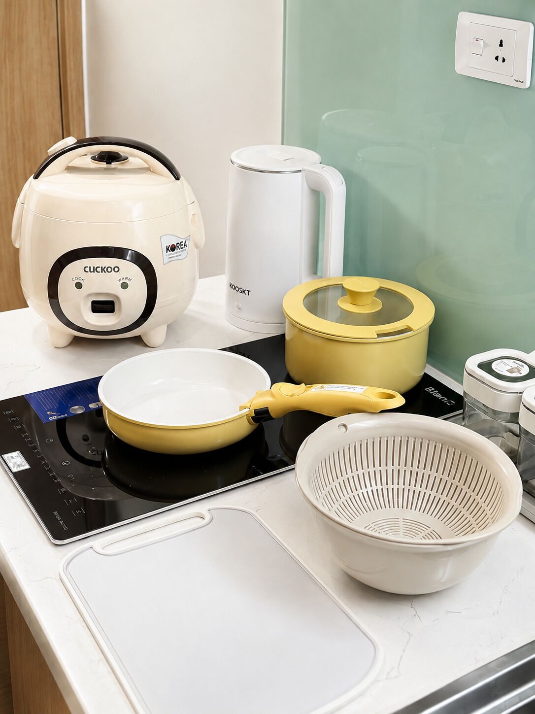 A kitchen counter with a rice cooker, a pot, a frying pan, a colander, and a blender.