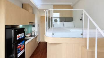 Habitación de hotel compacta con cama, kitchenette y baño pequeño.