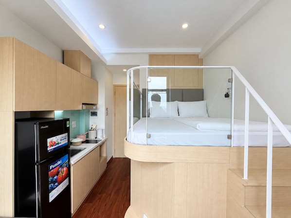 A compact hotel room with a bed, kitchenette, and a small bathroom.
