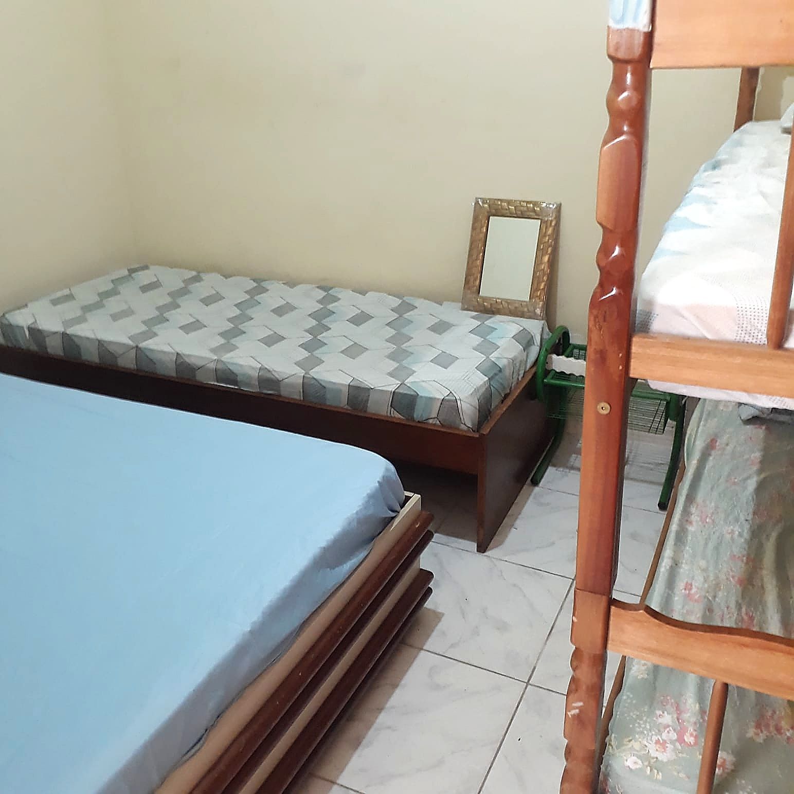 Quarto com uma cama de solteiro, cabeceira de madeira, mesa de cabeceira e uma cadeira verde.