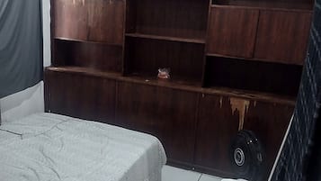 Quarto com cama, cadeira branca, mesa pequena e um amplo aparador de madeira.