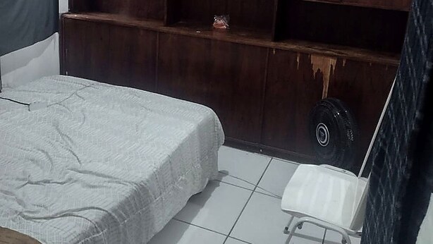 A bedroom with a bed, a white chair, a small table, and a large wooden shelving unit. - Pousada Maanaim (Rio de Janeiro)