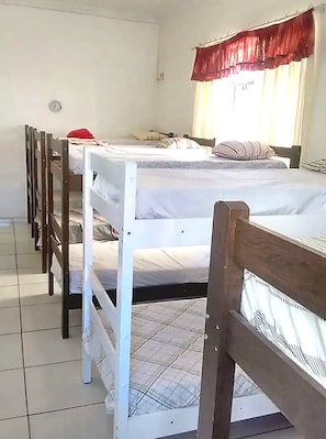 Un dormitori amb llits superposats, una finestra amb cortines i un terra d'rajola.