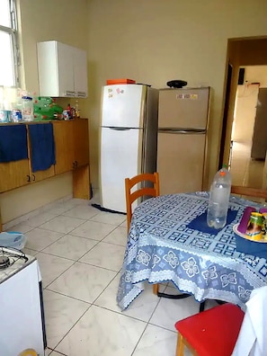 Una cuina compacta amb nevera, fogó de gas i taula amb mantell estampat.