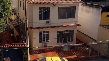 Um edifício de vários andares com telhado de telhas vermelhas, um táxi amarelo na frente e uma rua com carros estacionados.