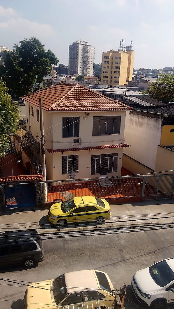 Un edifici de diversos pisos amb teules vermelles, un taxi groc al davant i un carrer amb cotxes aparcats.