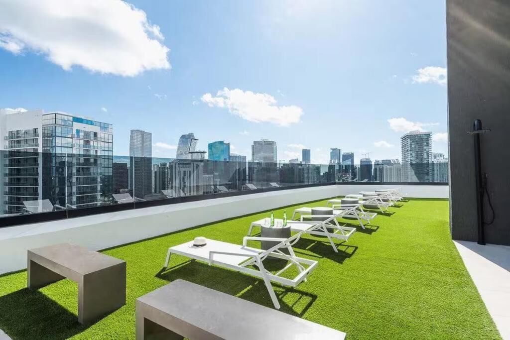Terraza en la azotea con césped artificial, sillones de descanso y mesas, con vistas a un horizonte urbano.
