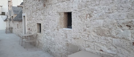 Un bâtiment en pierre avec une petite fenêtre et une table entourée de chaises.