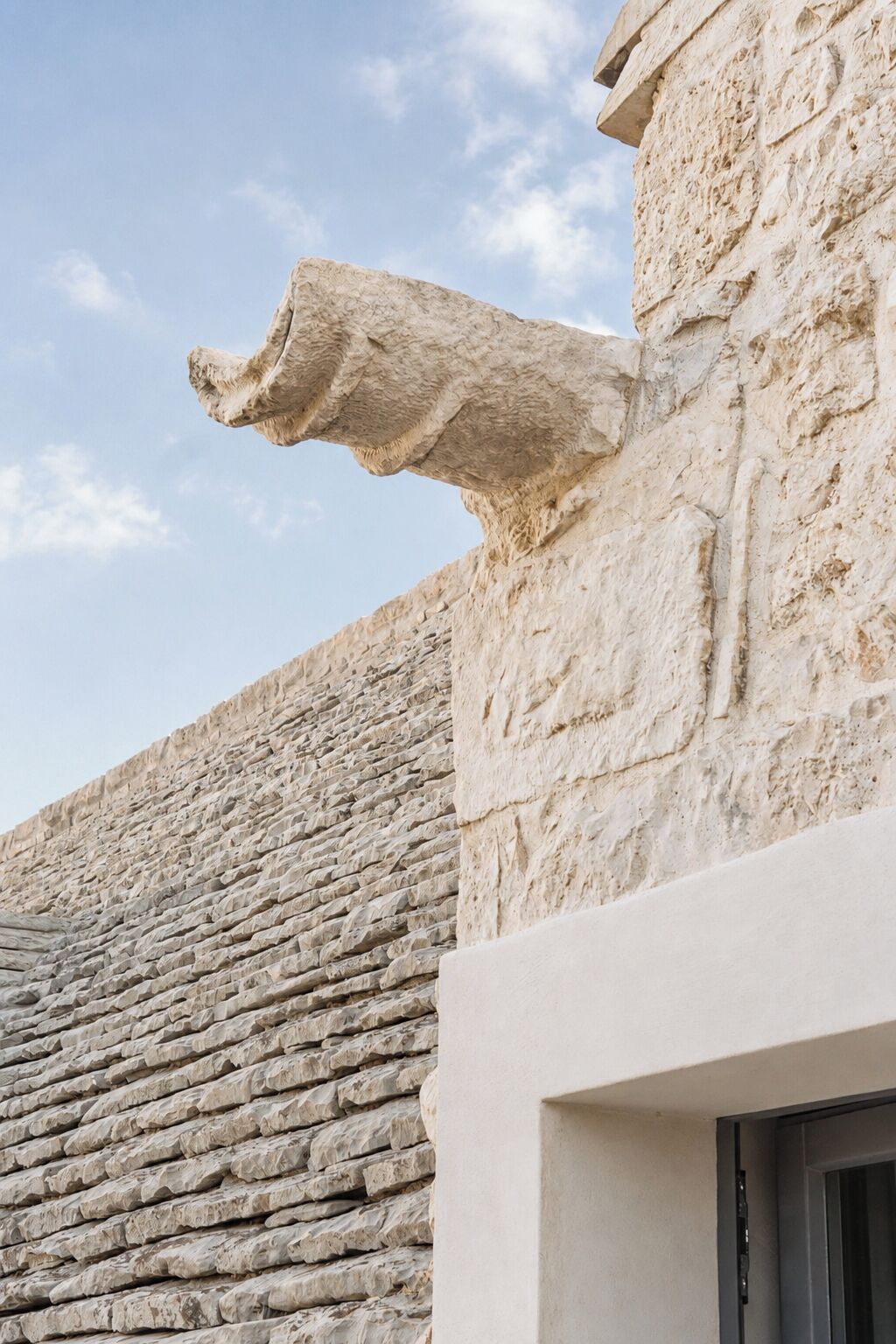 A stone wall with a rough texture and a modern building with a flat roof.