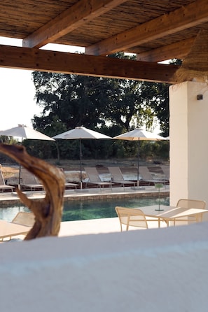 An outdoor pool area with lounge chairs and umbrellas, surrounded by trees. - Masseria Pastinaca Relais & Spa (Cisternino)