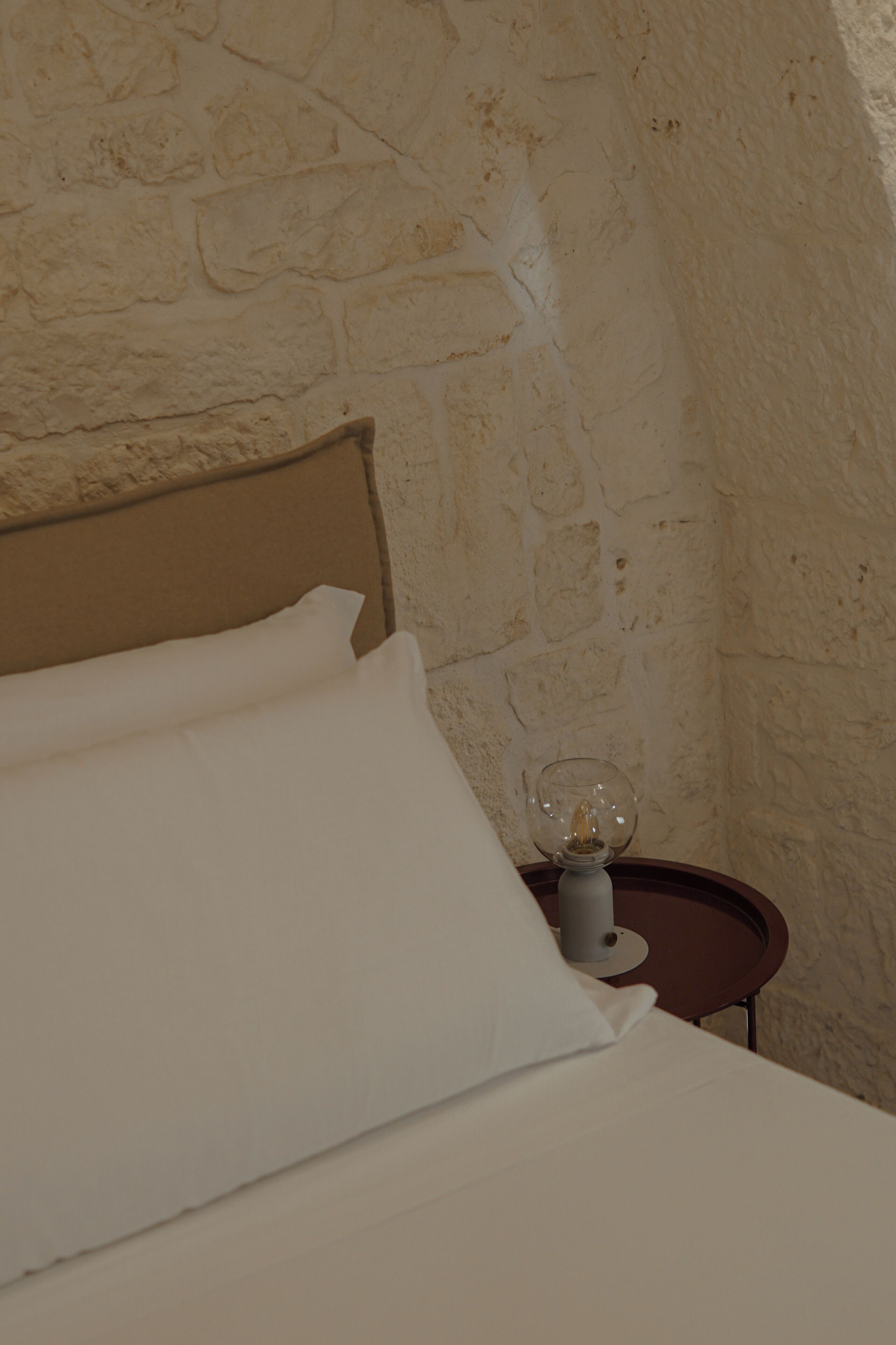 Una cama con sábanas blancas en una habitación con pared de piedra.