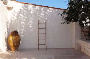 A ladder leaning against a wall with a large vase and a tree casting shadows. - Masseria Pastinaca Relais & Spa (Cisternino)