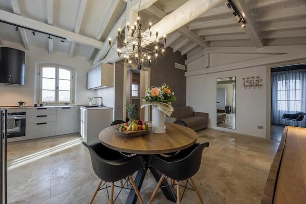 Une cuisine moderne avec des meubles blancs, un coin repas doté d’une table en bois et de chaises noires, et un lustre.