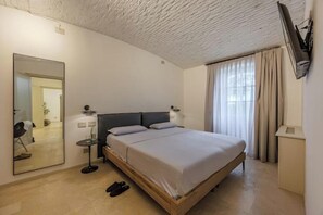 Et hotelværelse med en seng, et spejl, et lille bord og et tv ophængt på væggen.