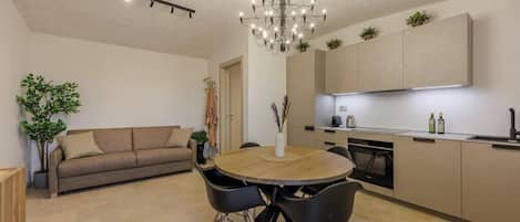 A modern kitchen with built-in appliances, a dining area with a round table and chairs, and a living room with a sofa and a plant.