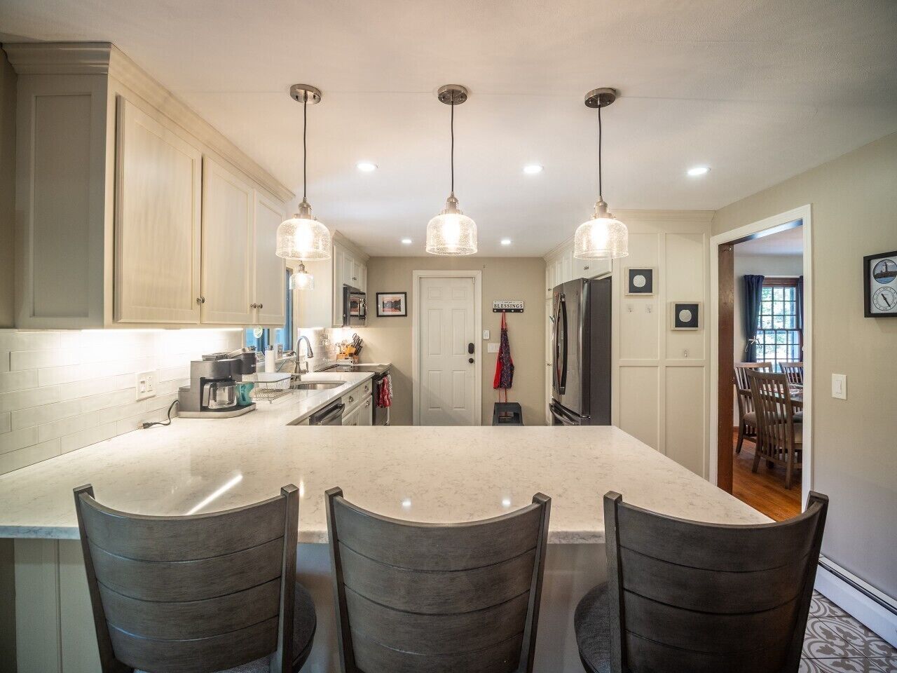 A kitchen with a large island, pendant lights, and a dining area with chairs.