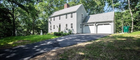Une maison à deux étages avec un garage, entourée d’une cour verdoyante et d’arbres.