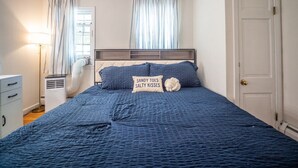 A bedroom with a bed, a bedside table, a lamp, a heater, and a door. - Connecticut Beach Home (Old Lyme)