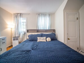 Ein Schlafzimmer mit Bett, Nachttisch, Lampe, Heizung und einer Tür.