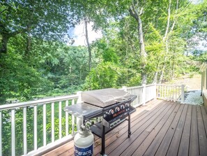 Ein Grill mit Holzbalkon und weißer Reling, umgeben von üppigem Grün.
